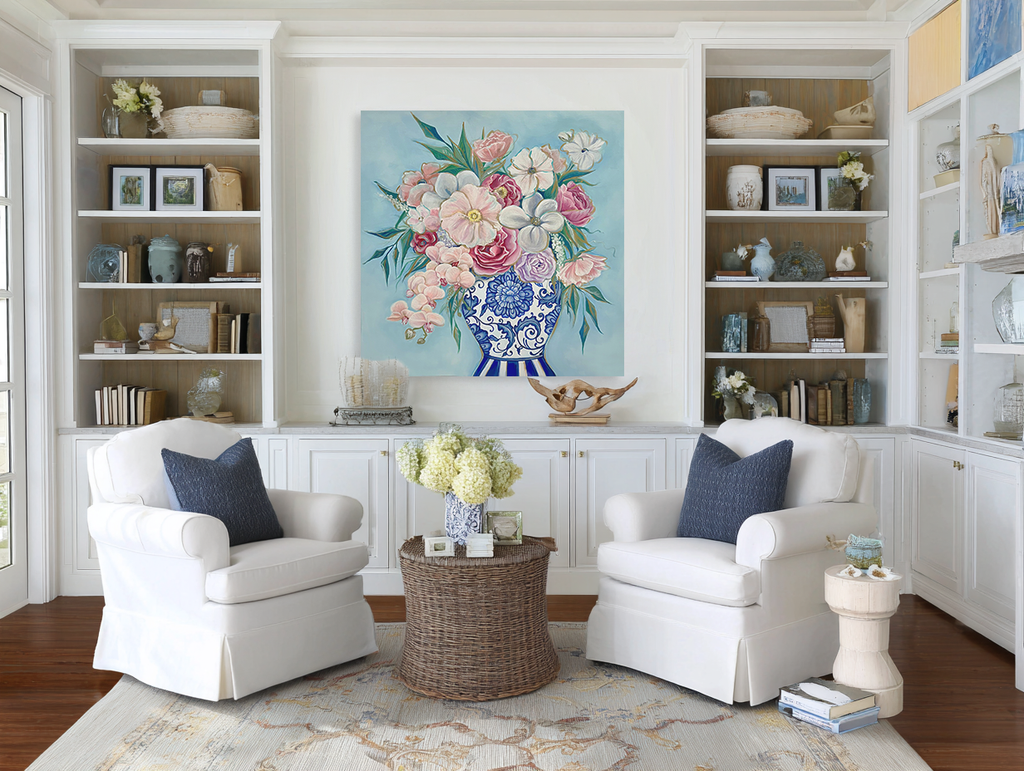 Living room with white armchairs, a floral painting, and bookshelves.