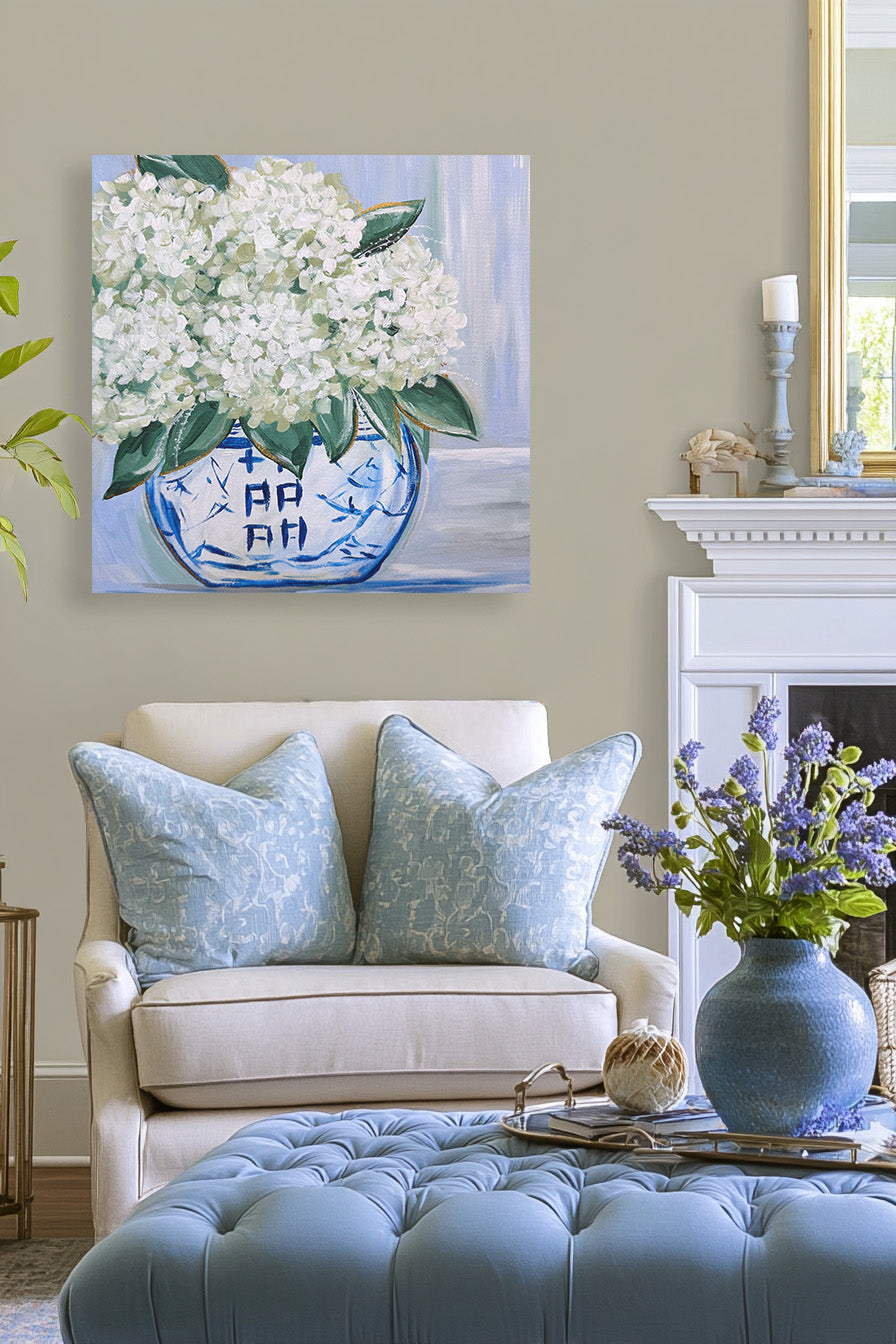 Living room with a painting of white flowers on the wall, a sofa with blue pillows, and a vase with purple flowers on a table.