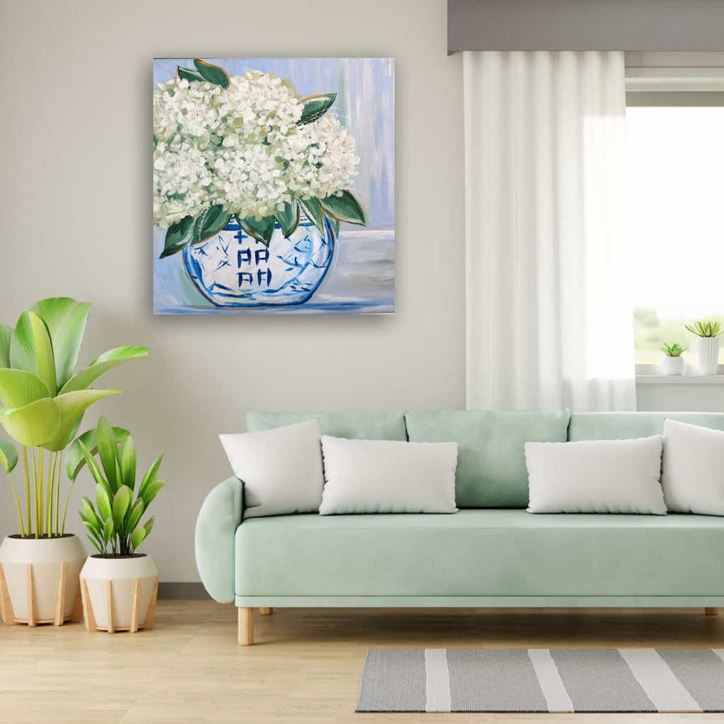 Living room with a light green sofa, potted plants, and a painting of white flowers in a blue vase on the wall.